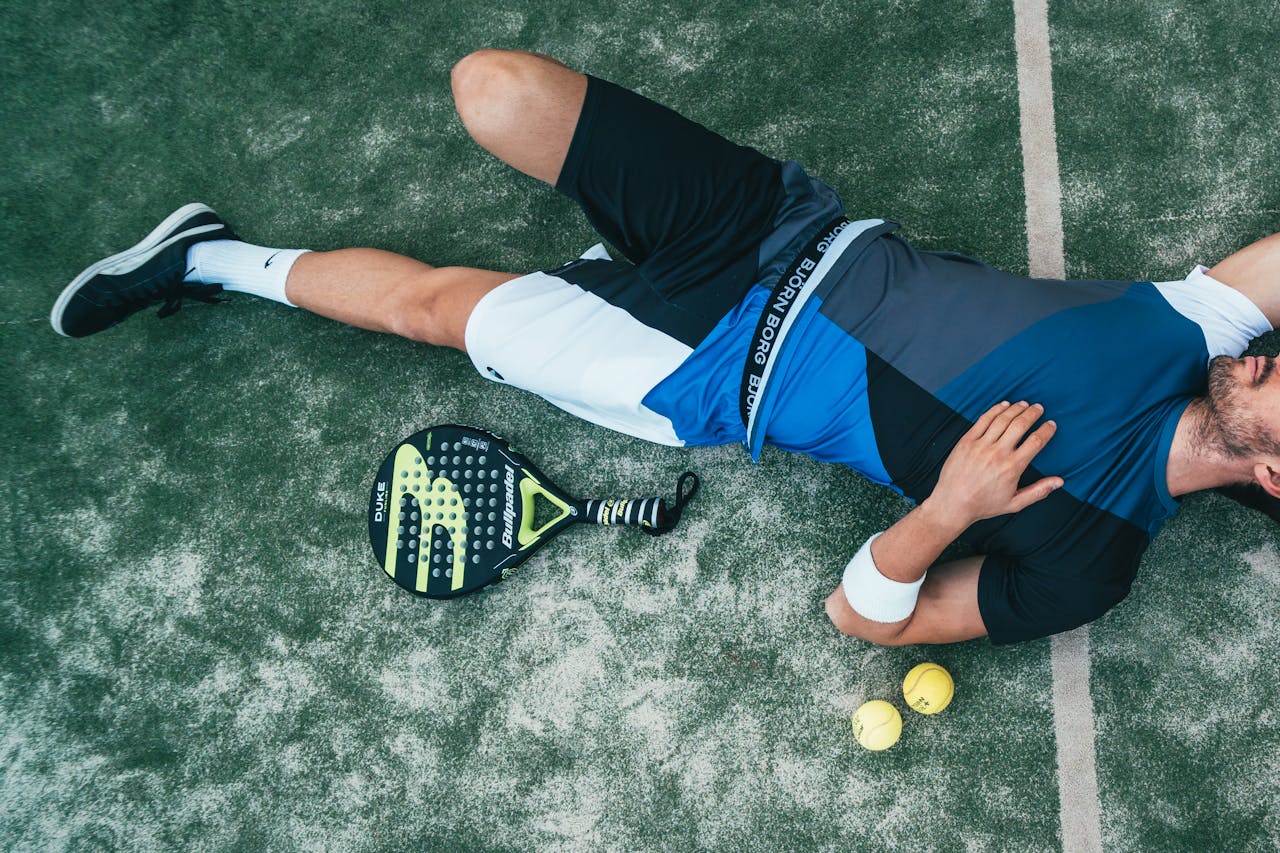 About Tired young athlete resting on padel court with racket and balls nearby.